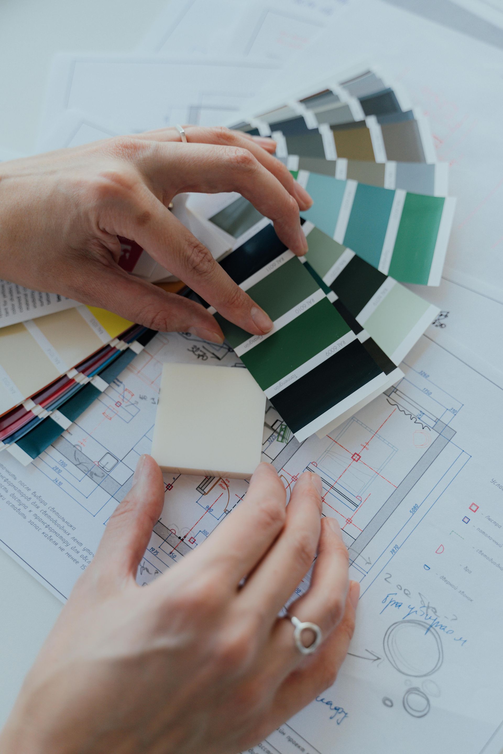 Hands selecting green and gray fabric swatches over fashion design sketches on a desk