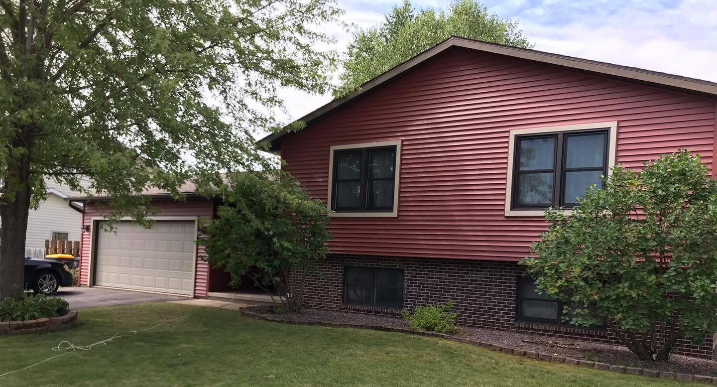Suburban house with red siding, dark stone base, and a garage beside a green lawn and trees