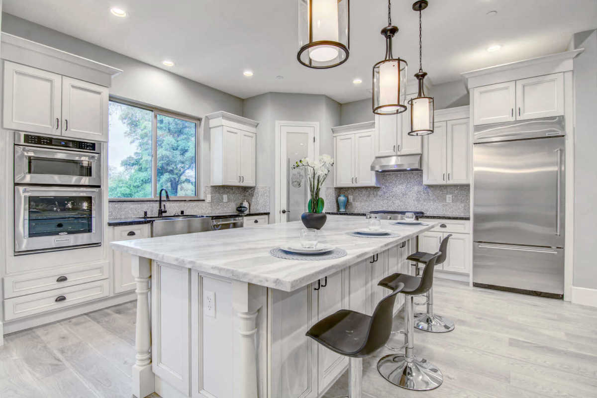 Modern white kitchen with marble island, stainless steel appliances, and pendant lights