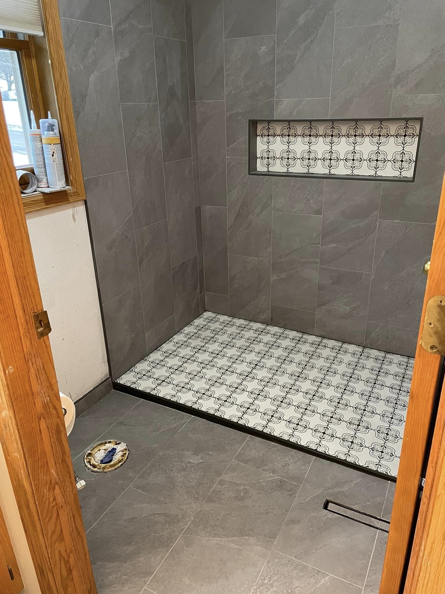 Small tiled bathroom with a shower area, gray walls, and a patterned shower mat.