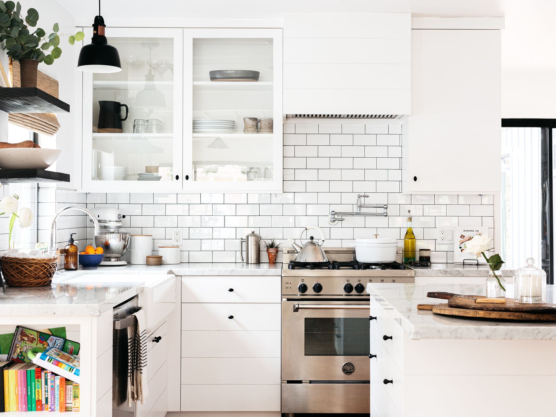Bright white kitchen with subway tile, stainless stove, glass cabinets, and wooden island.