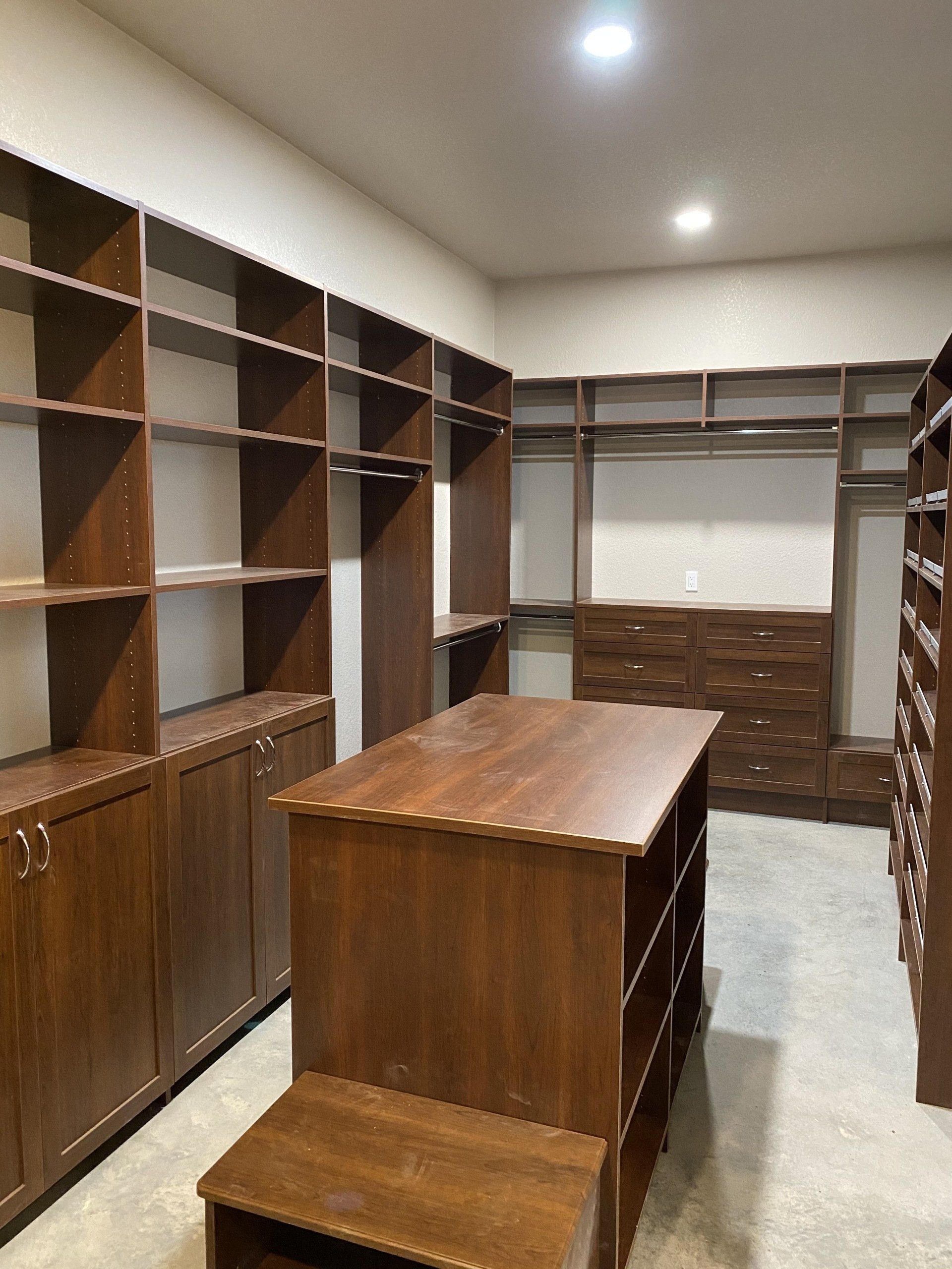 A walk in closet with lots of shelves and a table in the middle.