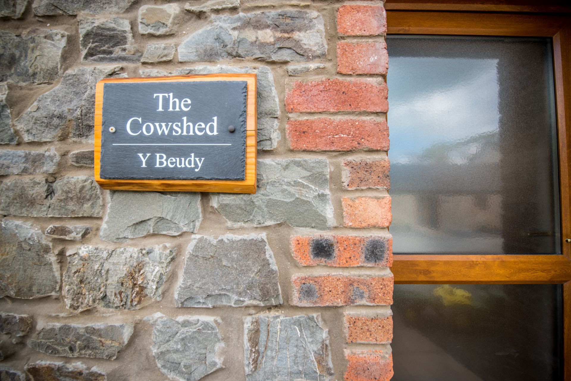 Exterior entrance of The Cowshed at Green Grove Barns with traditional stone wall and sign.