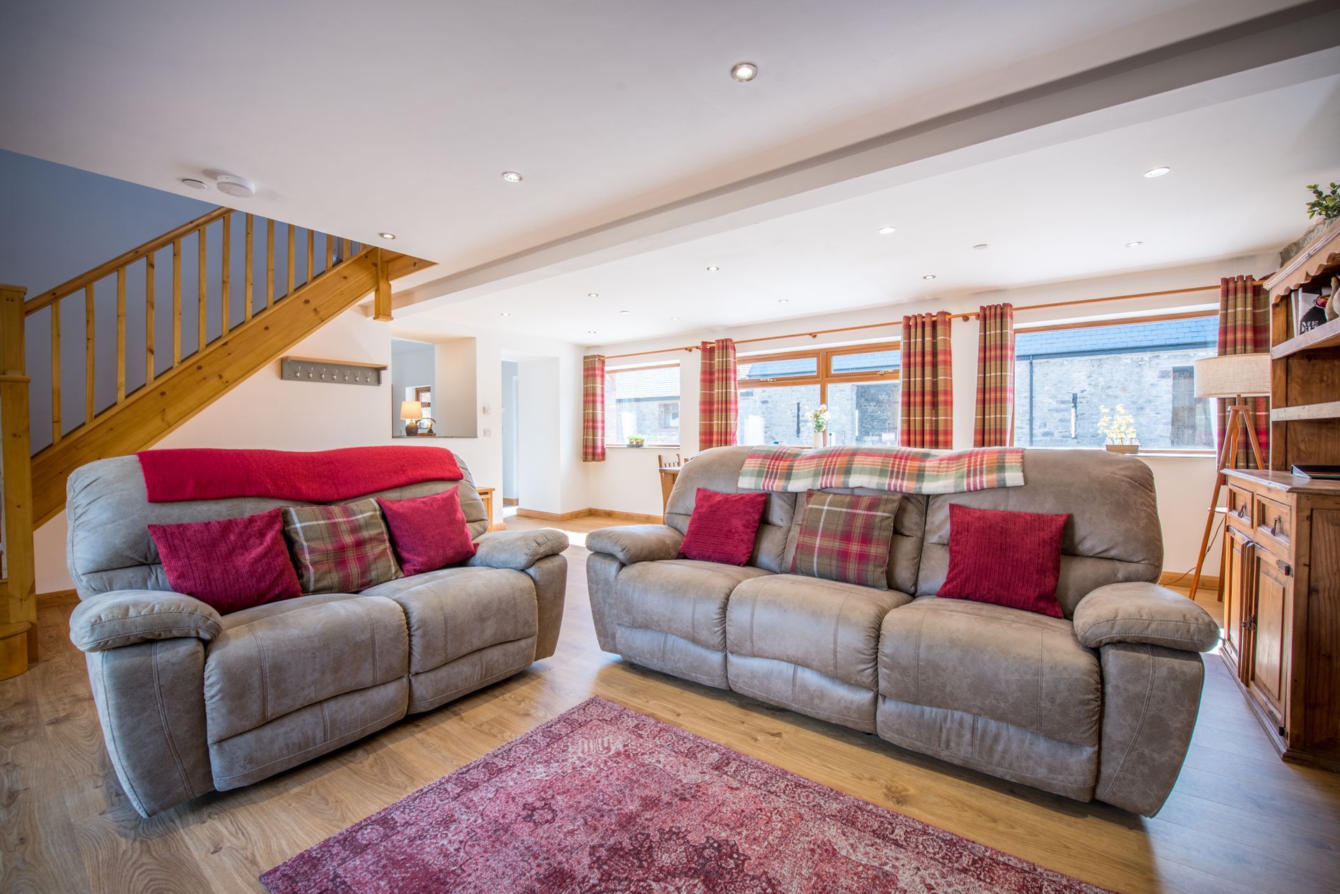 Living room at The Coach House with red sofas, exposed stone wall, and countryside views.