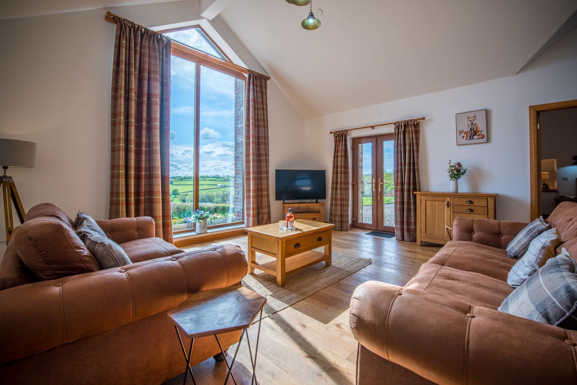 Living room at The Cowshed with comfy sofas, large windows and natural light.