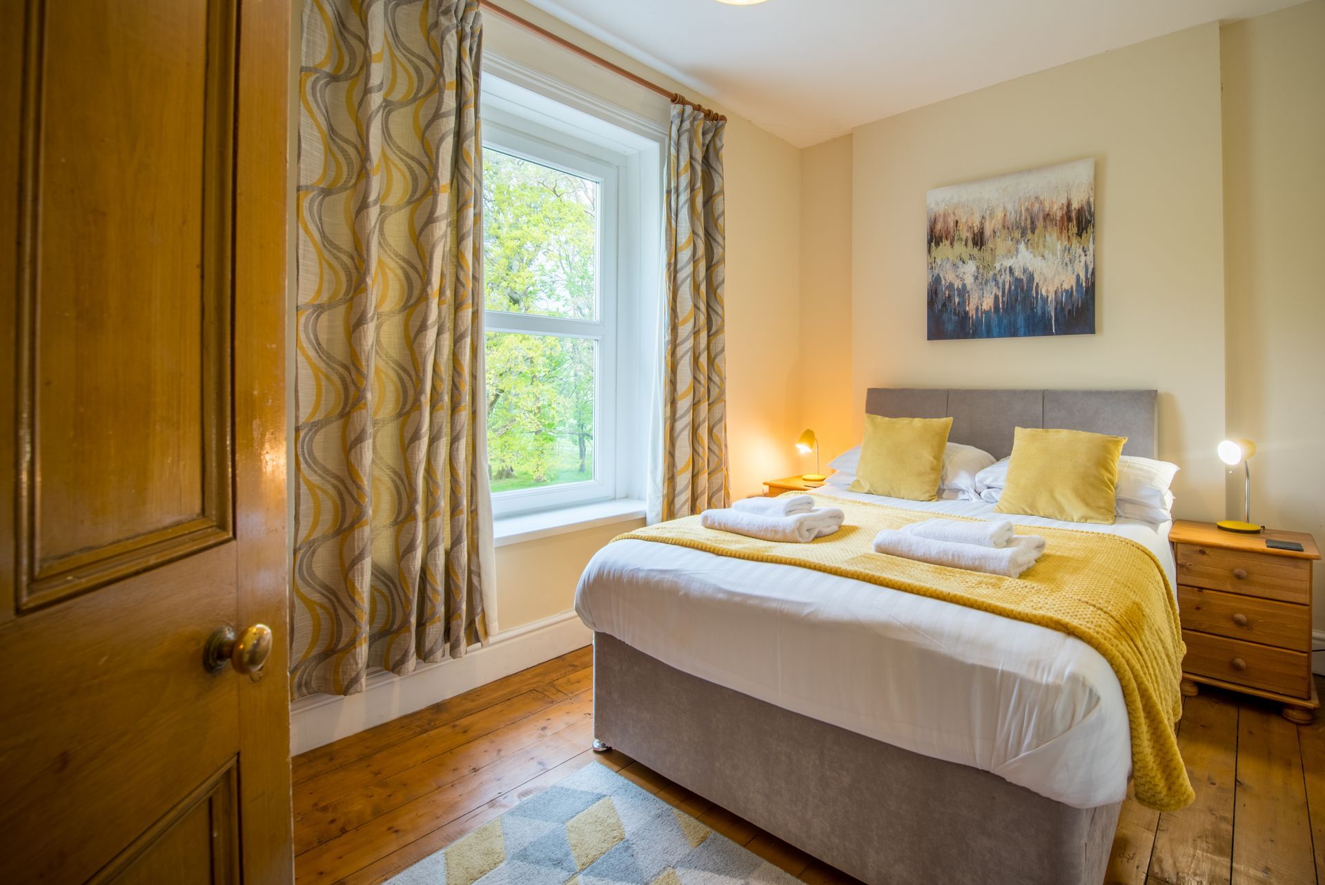 Bedroom in The Farmhouse with yellow accents and countryside view through window.