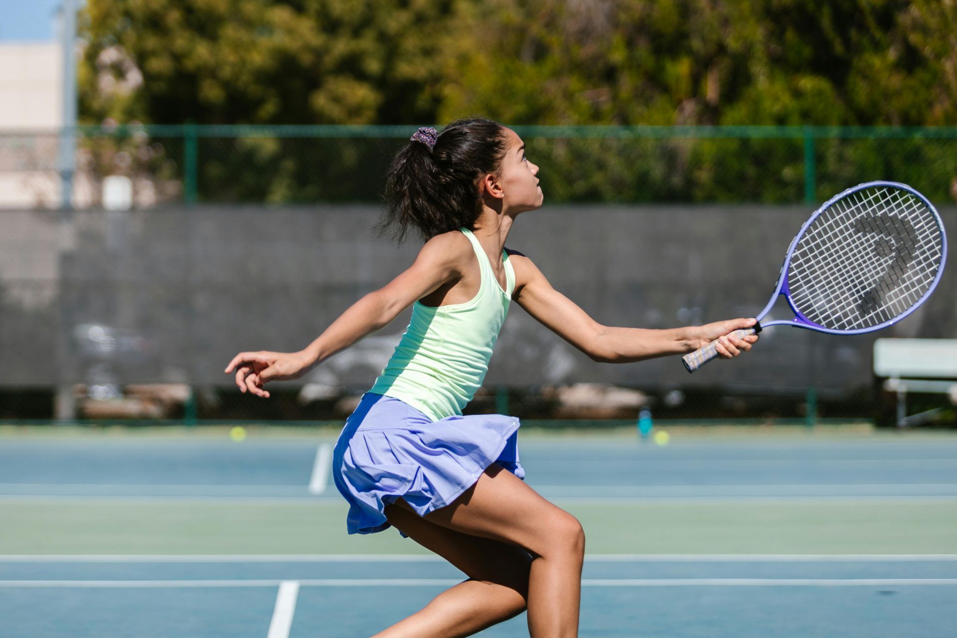 Girl in tennis attire swings a racket on a blue court.