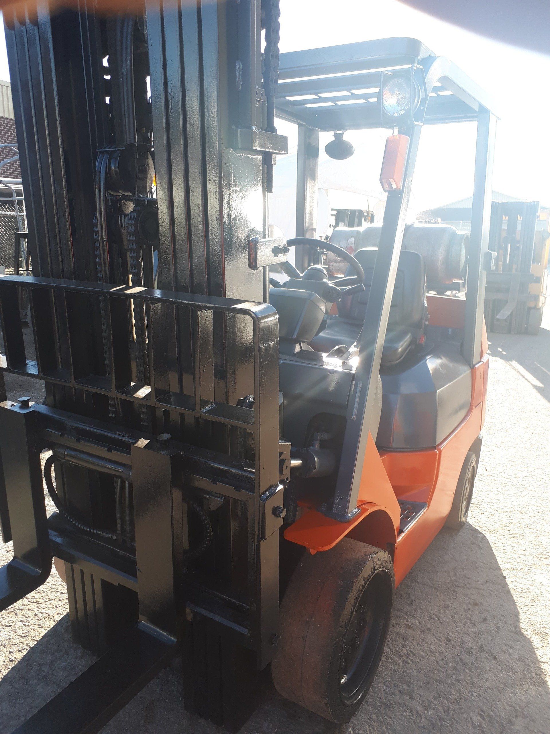 An orange and black forklift is parked on a gravel road