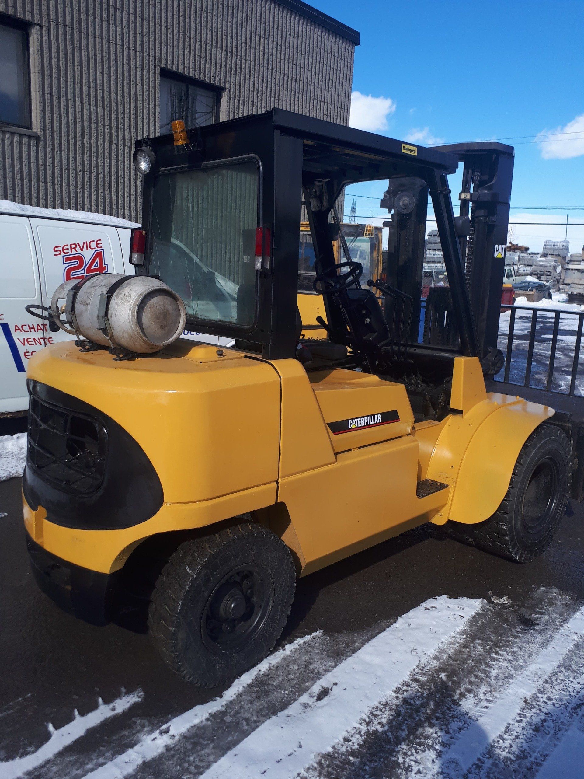 A yellow forklift is parked in the snow in front of a building.