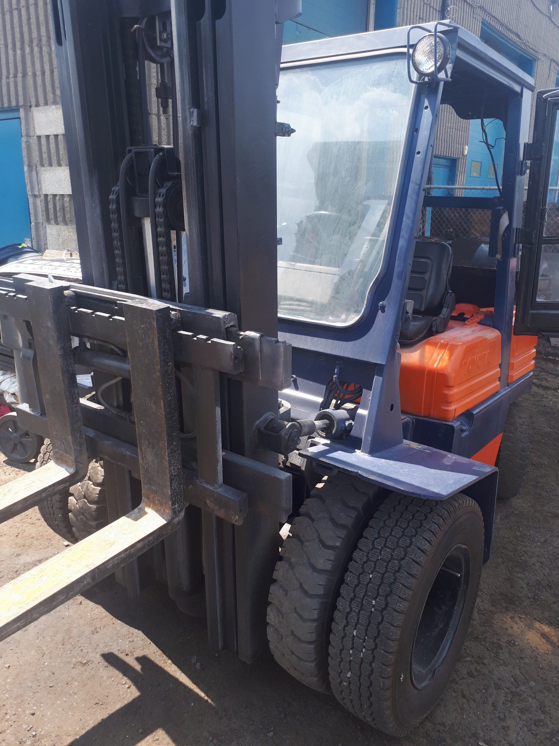 A forklift is parked in the dirt in front of a building.