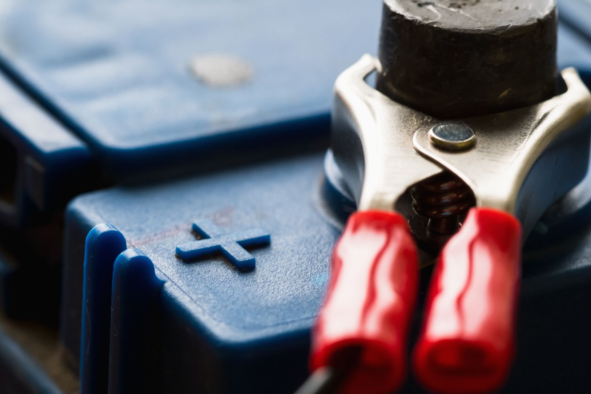 Gros plan sur une borne bleue de batterie de voiture avec une pince rouge de câble de démarrage positif fixée.