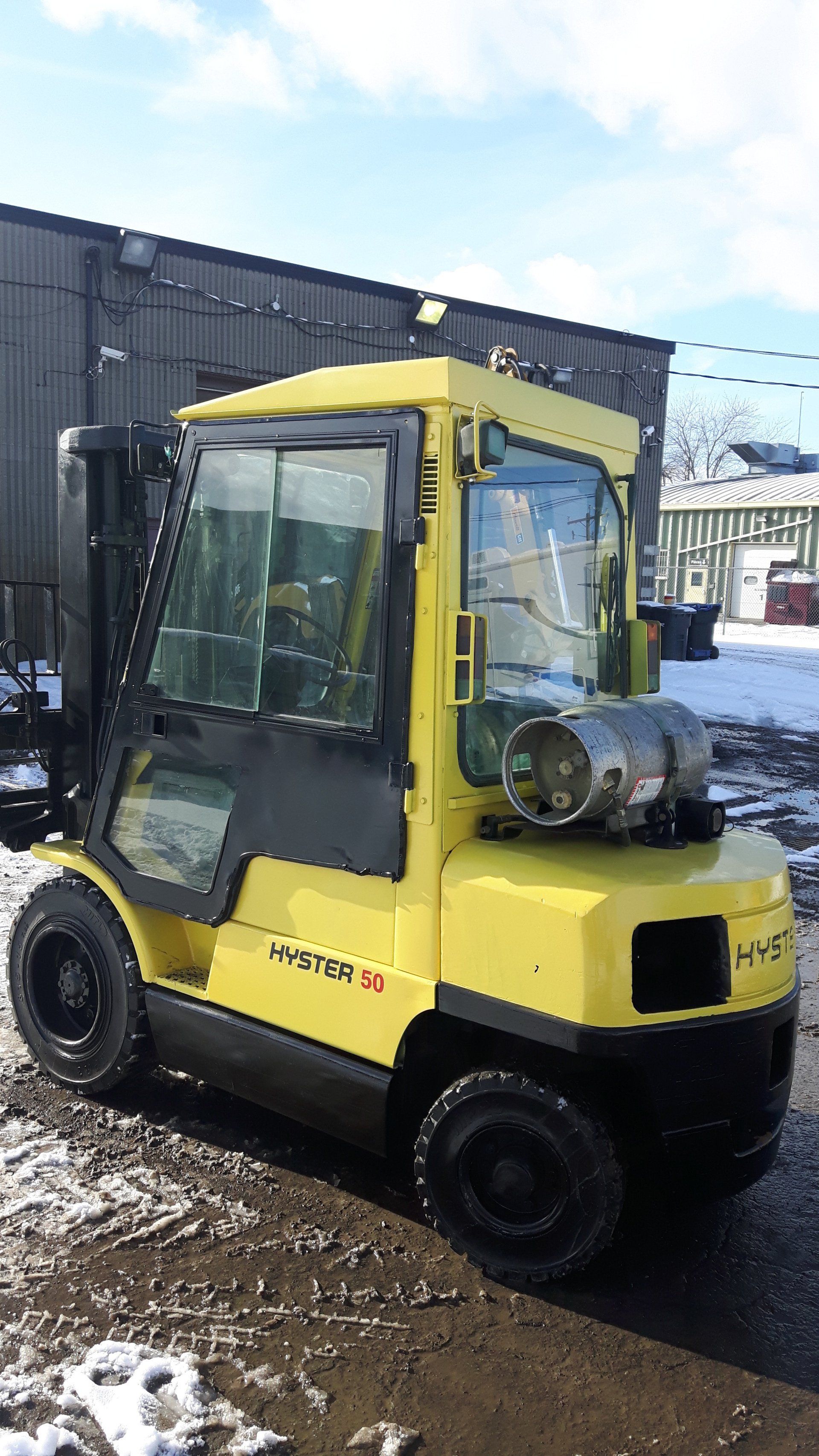 A yellow forklift is parked in the snow in front of a building.