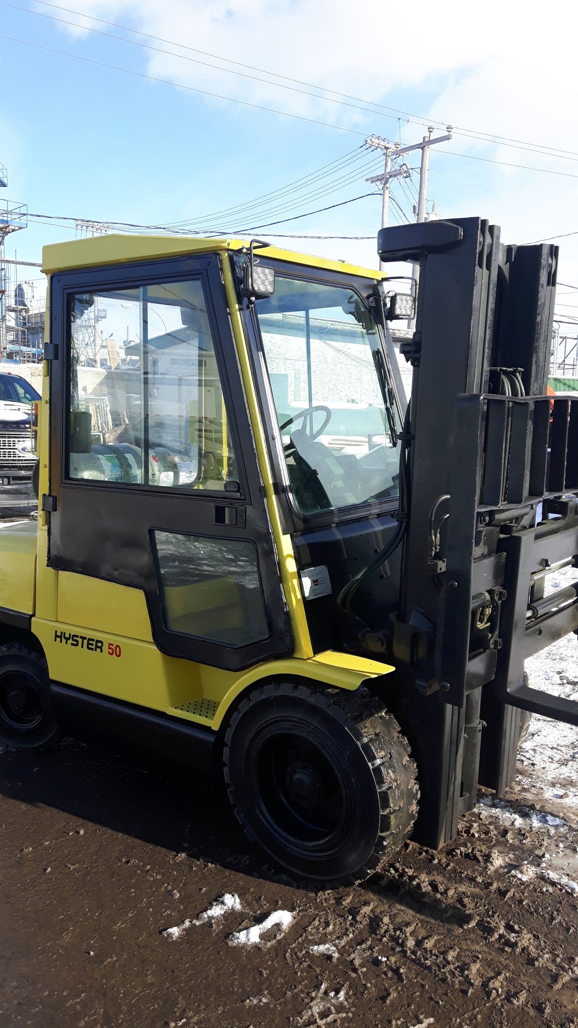 A yellow forklift is parked on the side of the road in the snow.