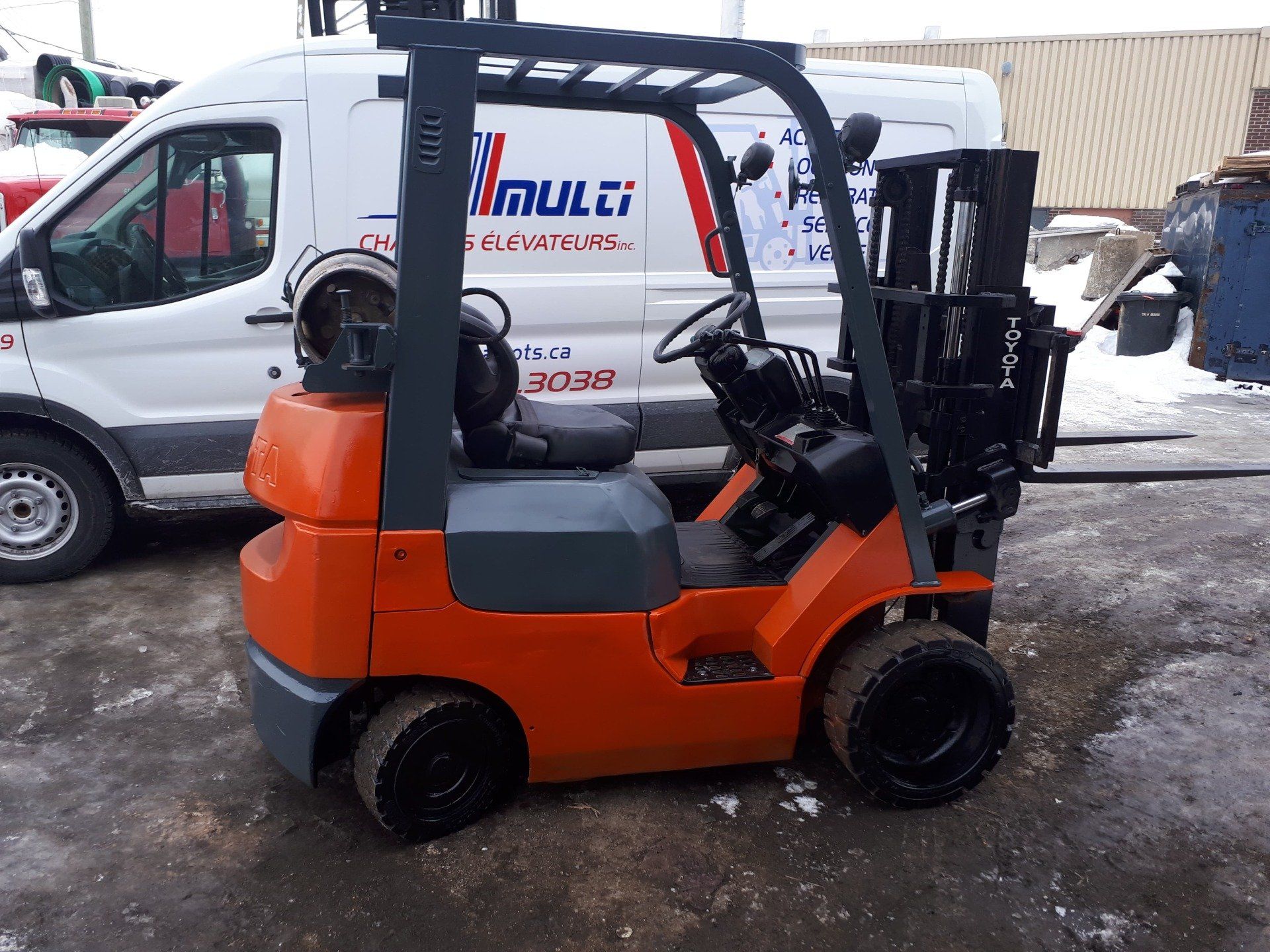 A forklift is parked in front of a white van with the word mult on it.