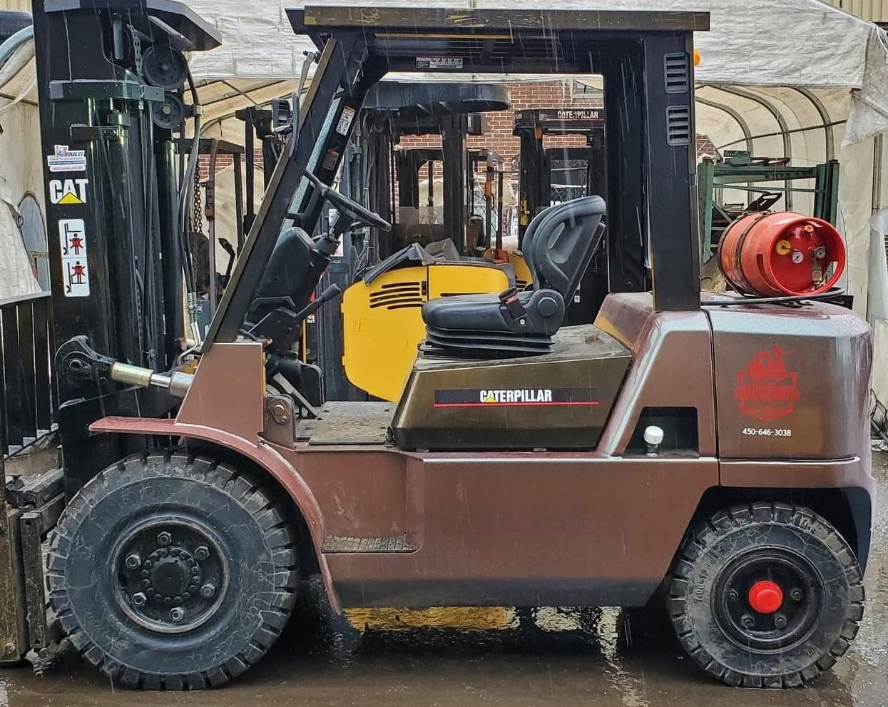 Chariot élévateur Caterpillar marron avec réservoir de propane, stationné à l'extérieur d'un bâtiment.
