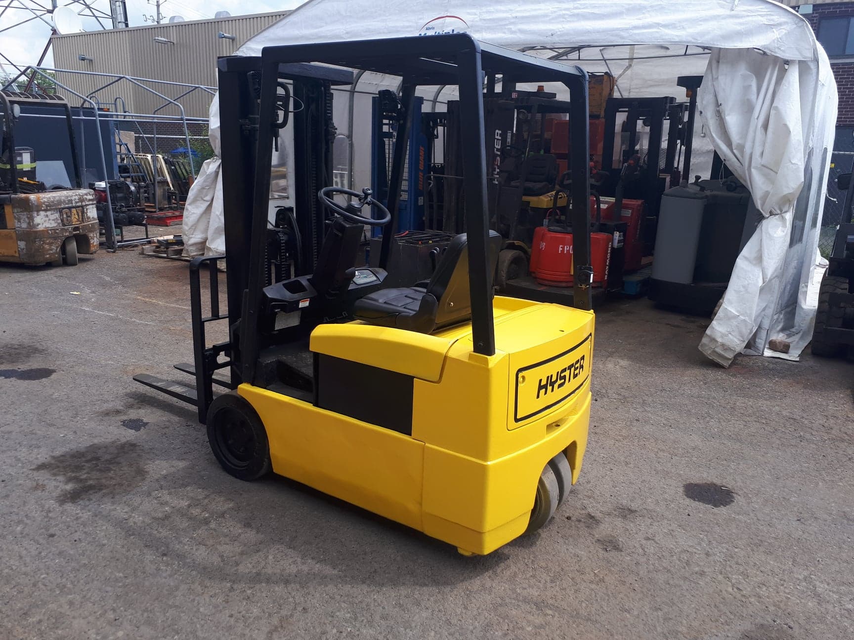 A yellow forklift is parked under a tent in a parking lot.