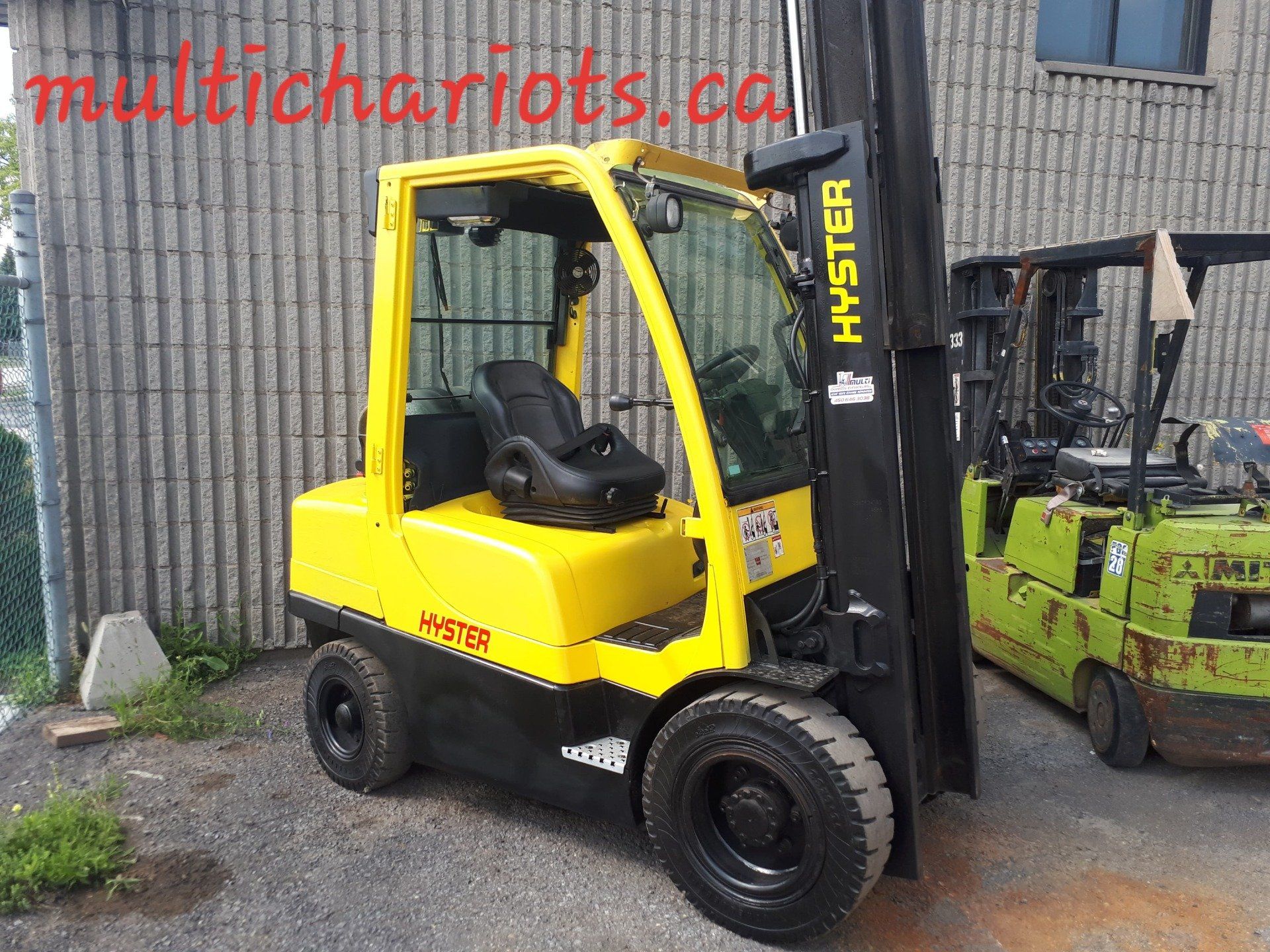 A yellow hyster forklift is parked in front of a building
