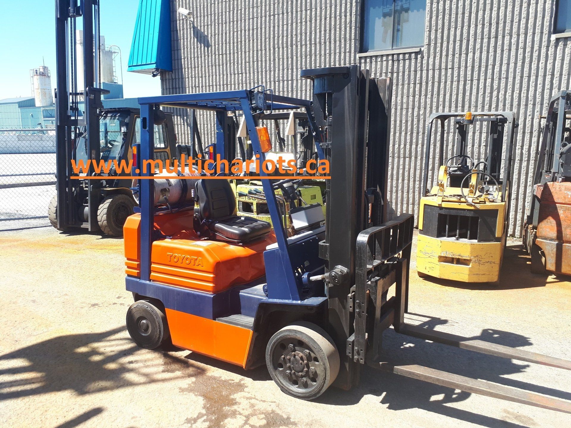 A blue and orange forklift is parked in front of a building