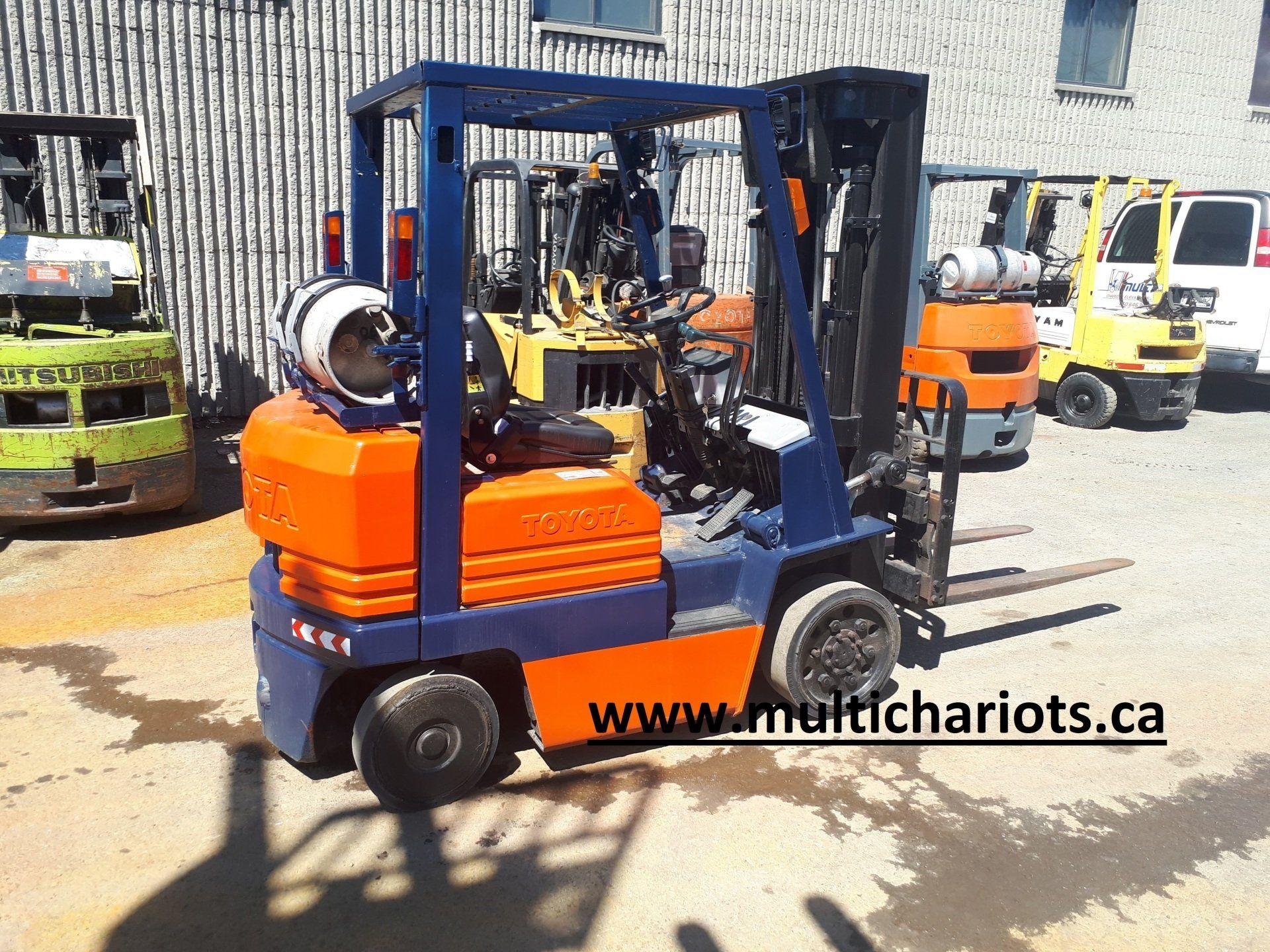 A blue and orange forklift is parked in front of a building