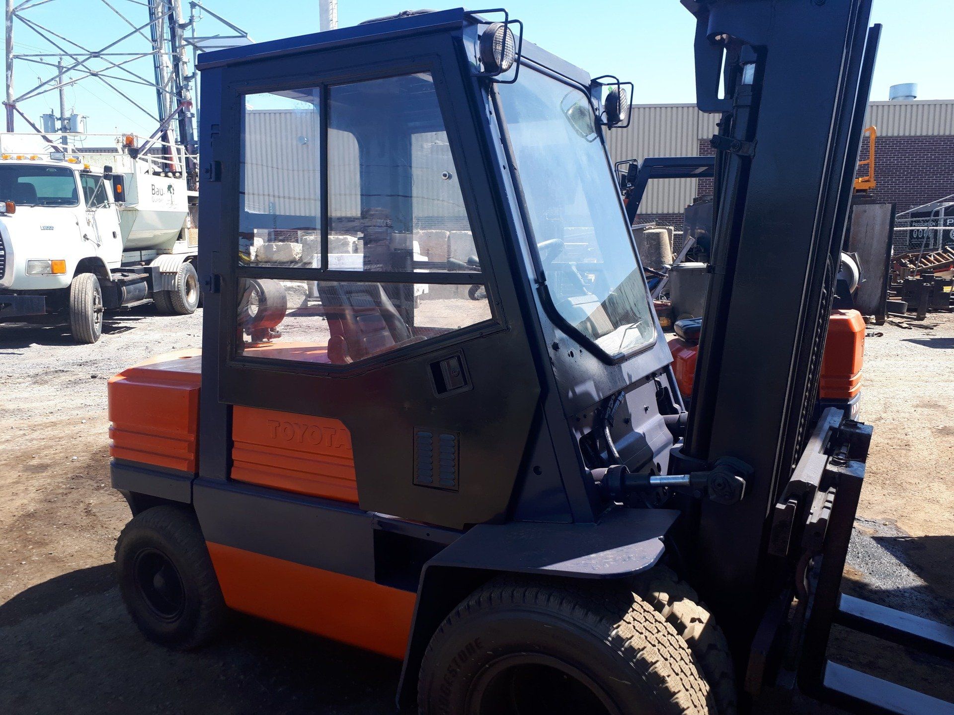 A black and orange forklift is parked in a dirt lot