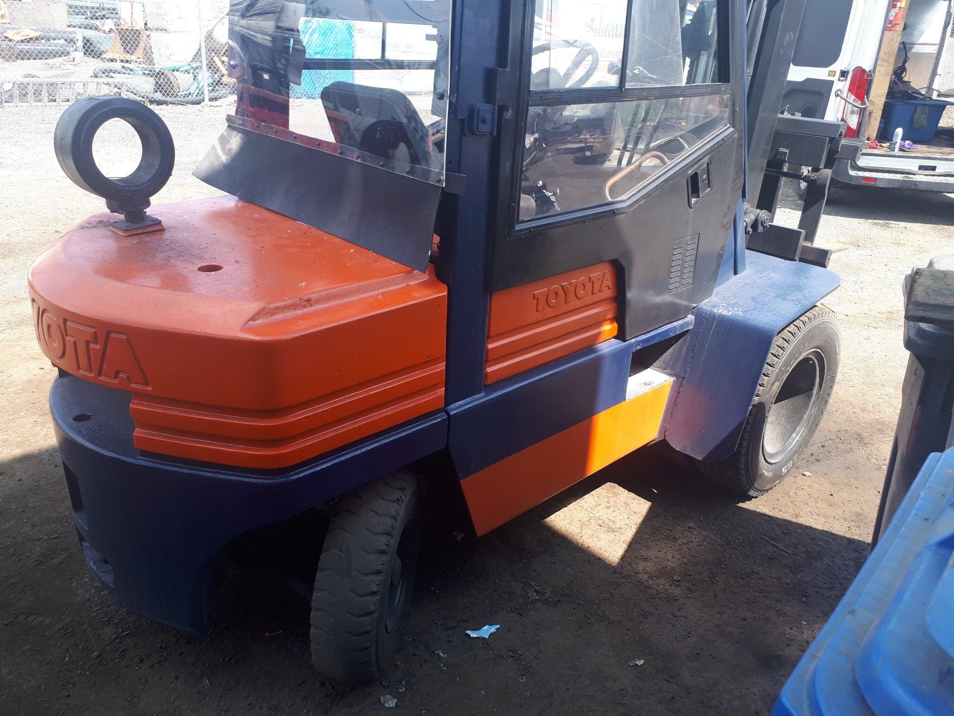 A blue and orange forklift is parked in a parking lot.