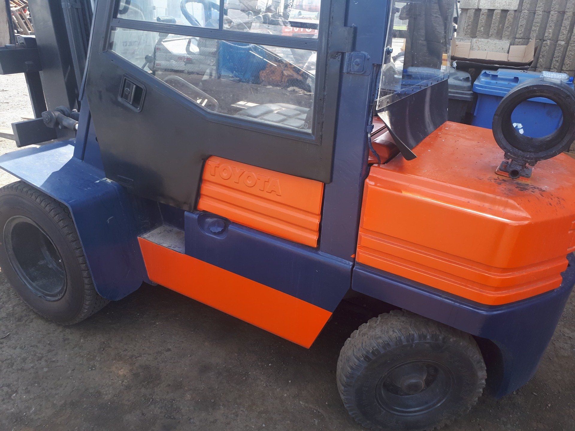A blue and orange forklift is parked on the side of the road.
