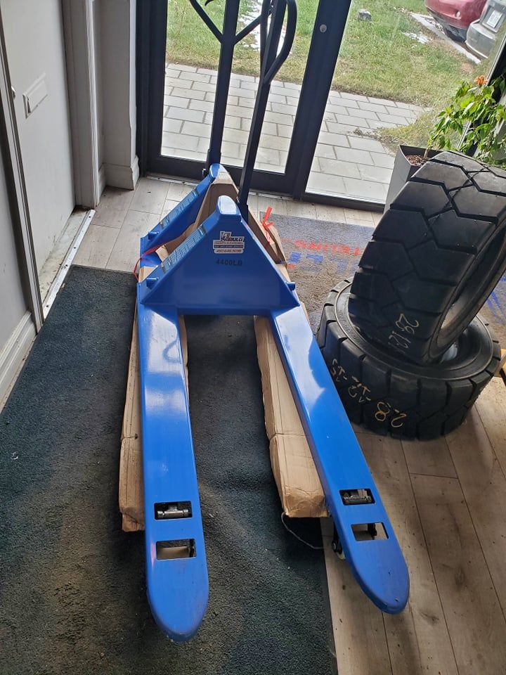 A blue forklift is sitting on a wooden pallet in a room.