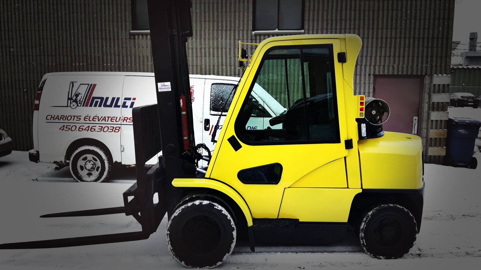 Chariot élévateur jaune sur la neige avec une camionnette en arrière-plan.