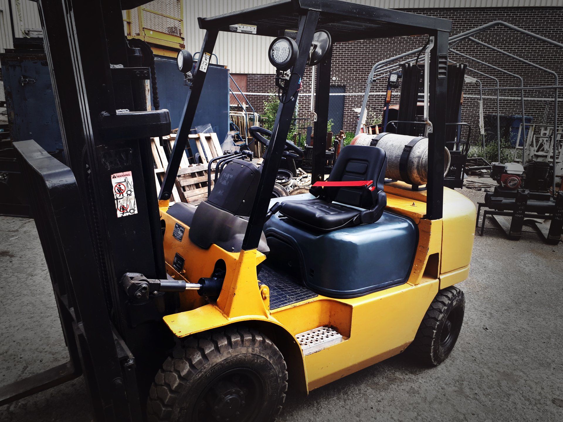 Chariot élévateur jaune avec cage de protection noire et réservoir de propane. Il est stationné à l'extérieur.