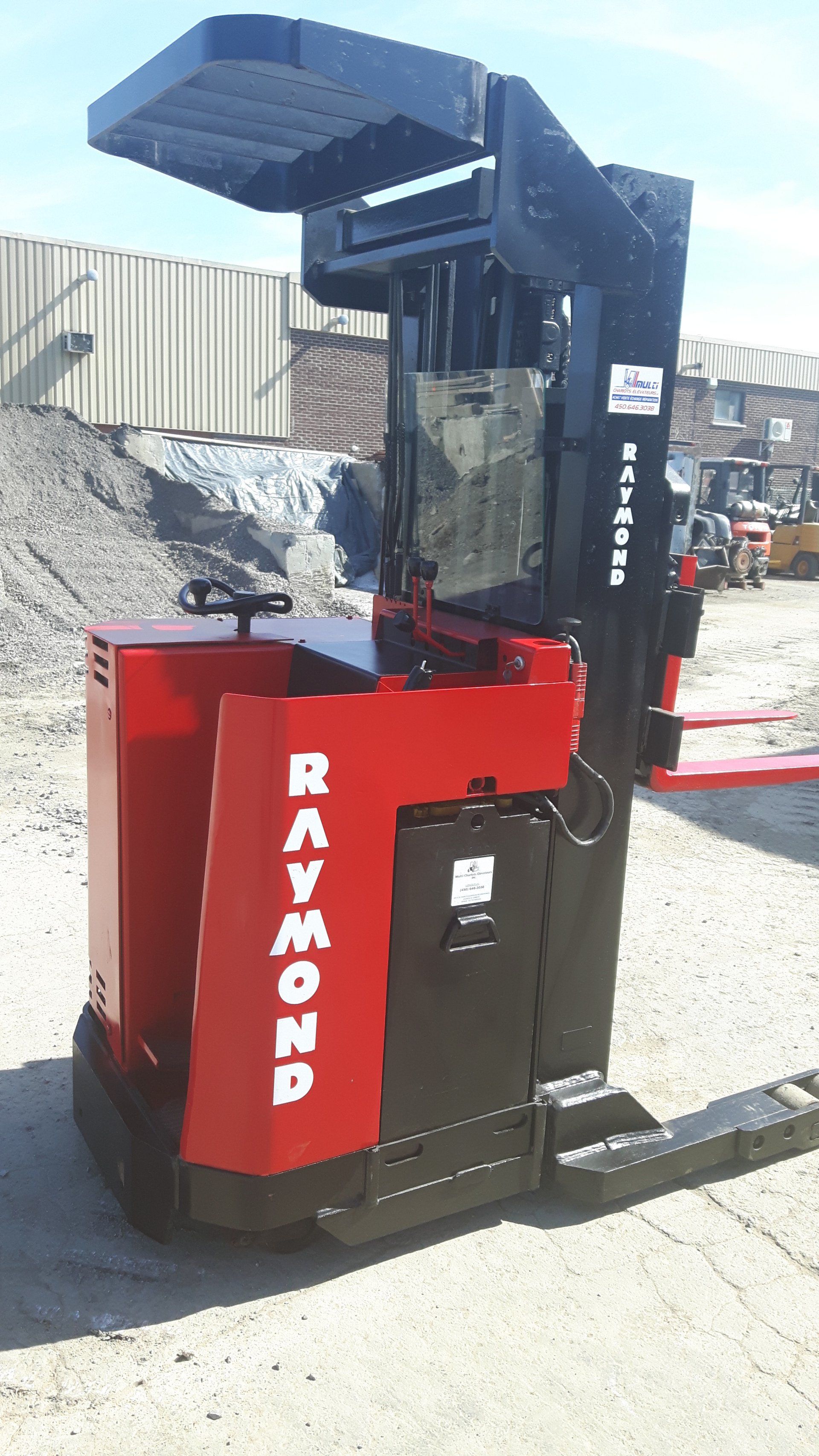 A red and black raymond forklift is parked in a gravel lot.
