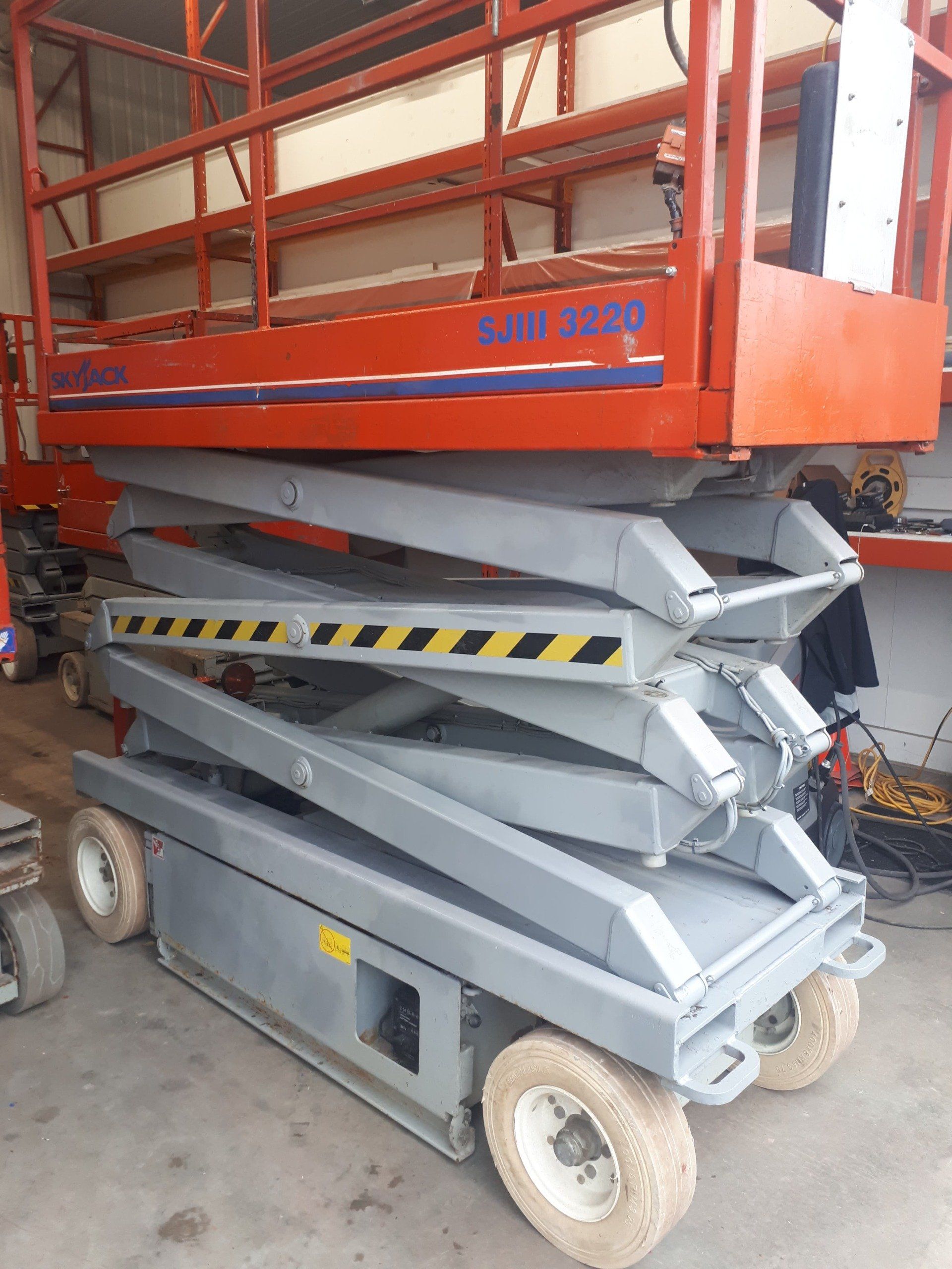 A gray and orange scissor lift is sitting in a garage.
