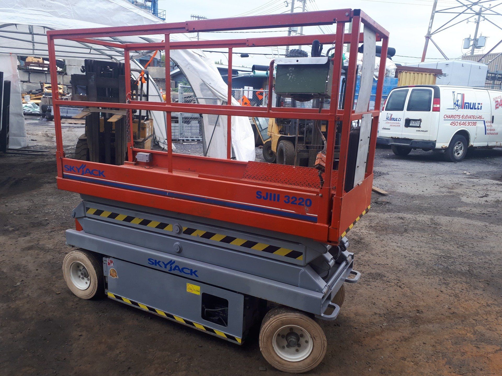 A red and gray scissor lift is parked in a parking lot.