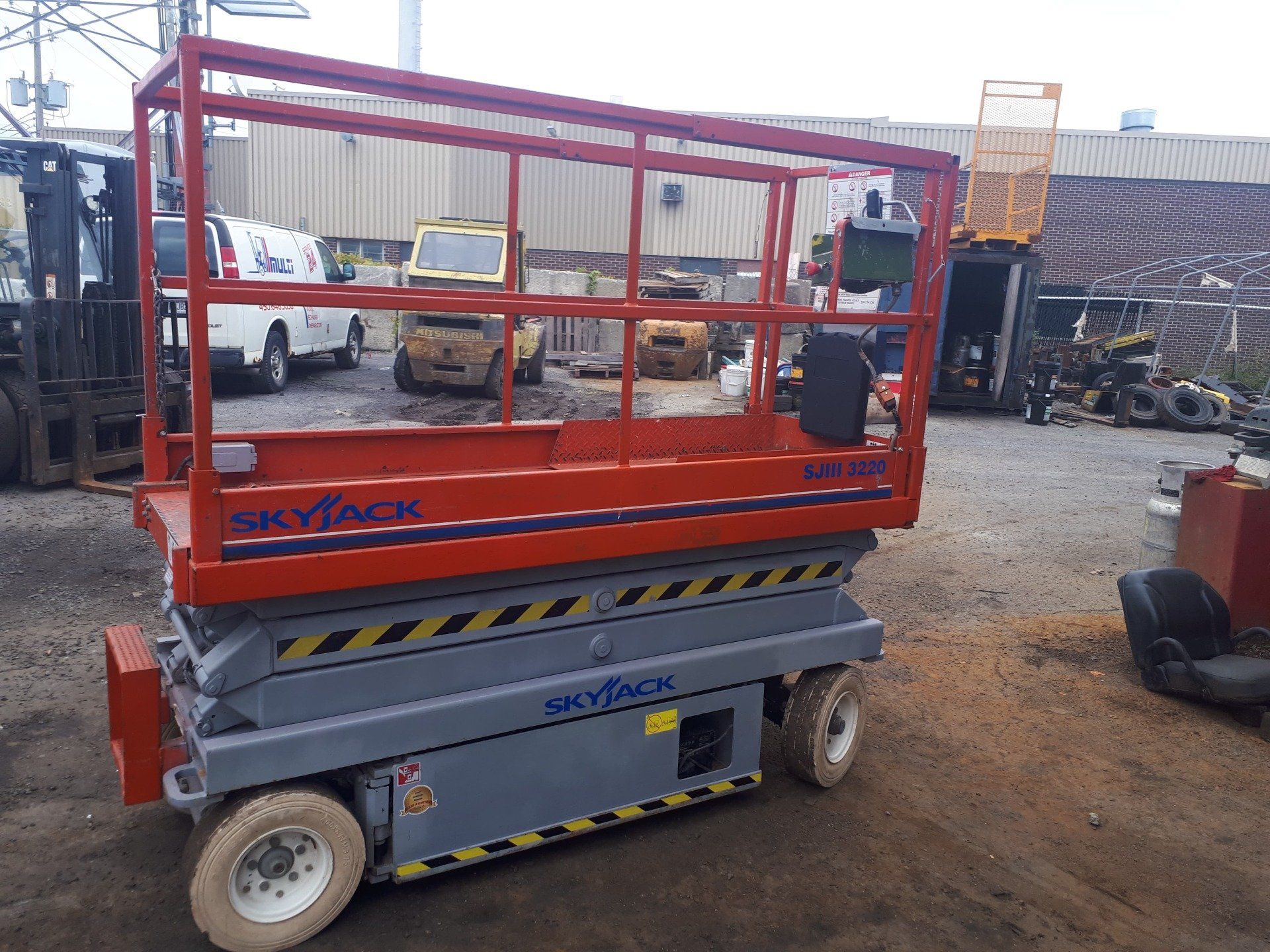 A scissor lift is parked in a parking lot in front of a building.