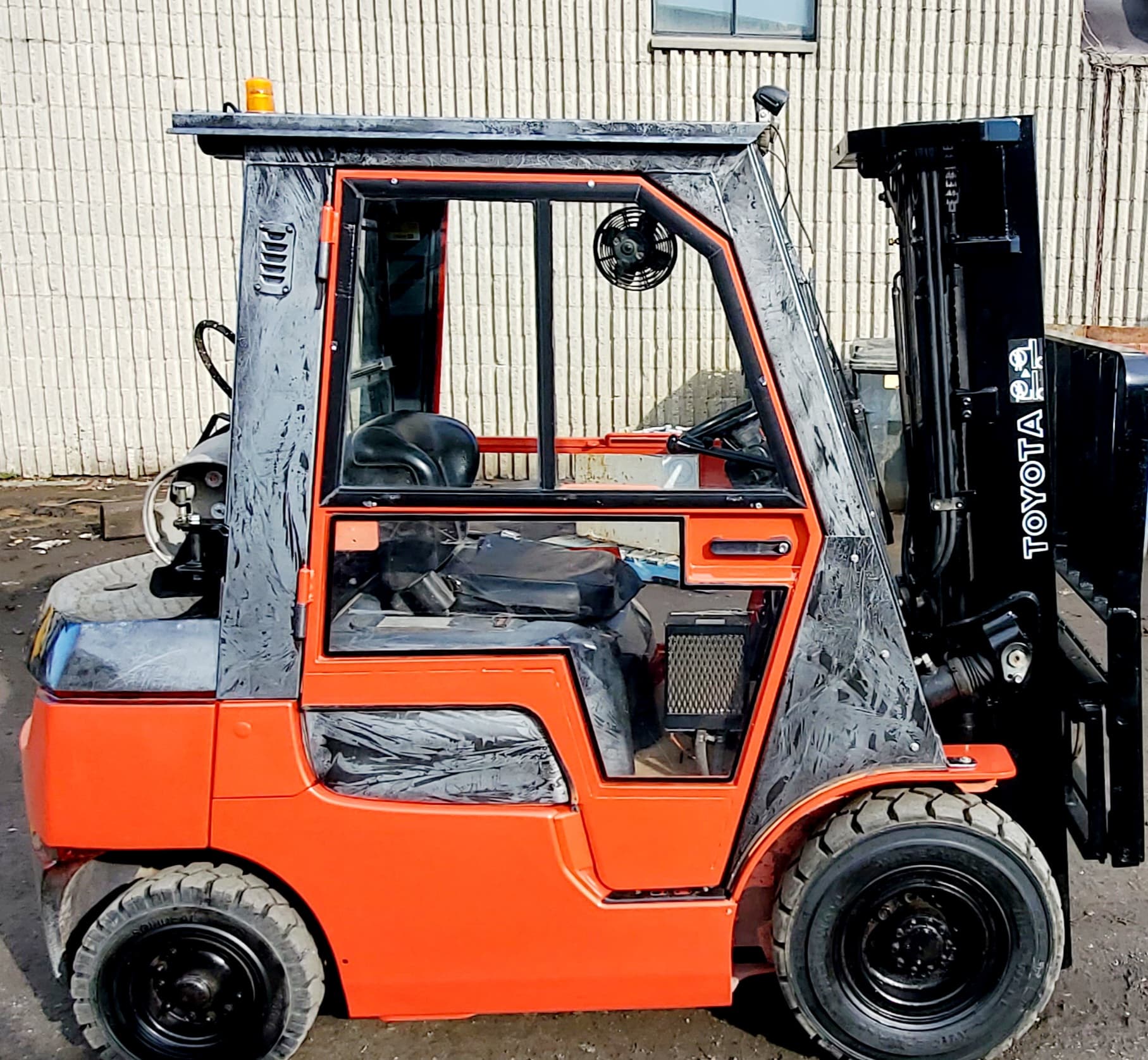 Chariot élévateur Toyota orange avec pneus et cabine noirs, stationné à l'extérieur.
