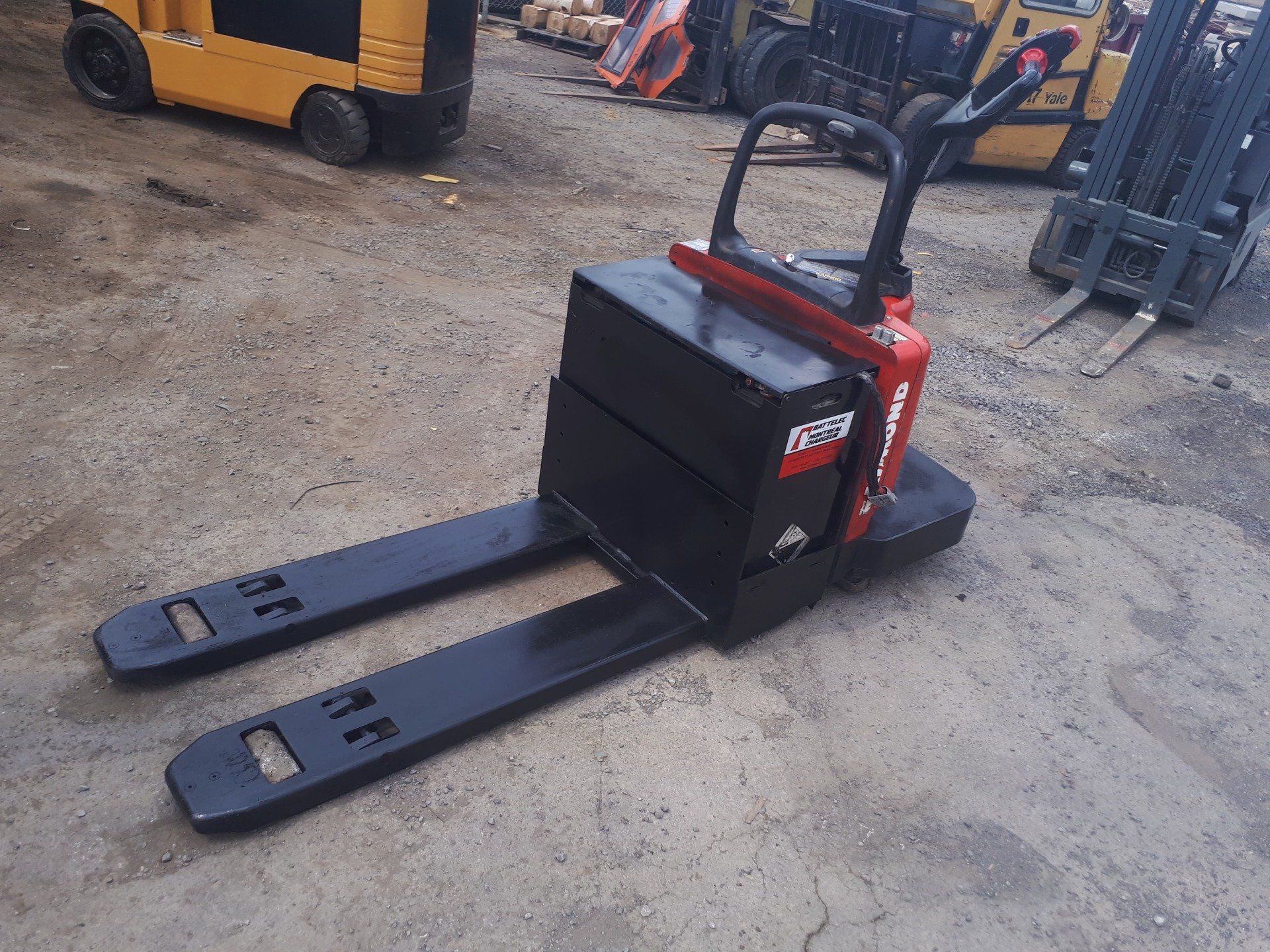 A forklift is parked in a parking lot next to a pallet truck.