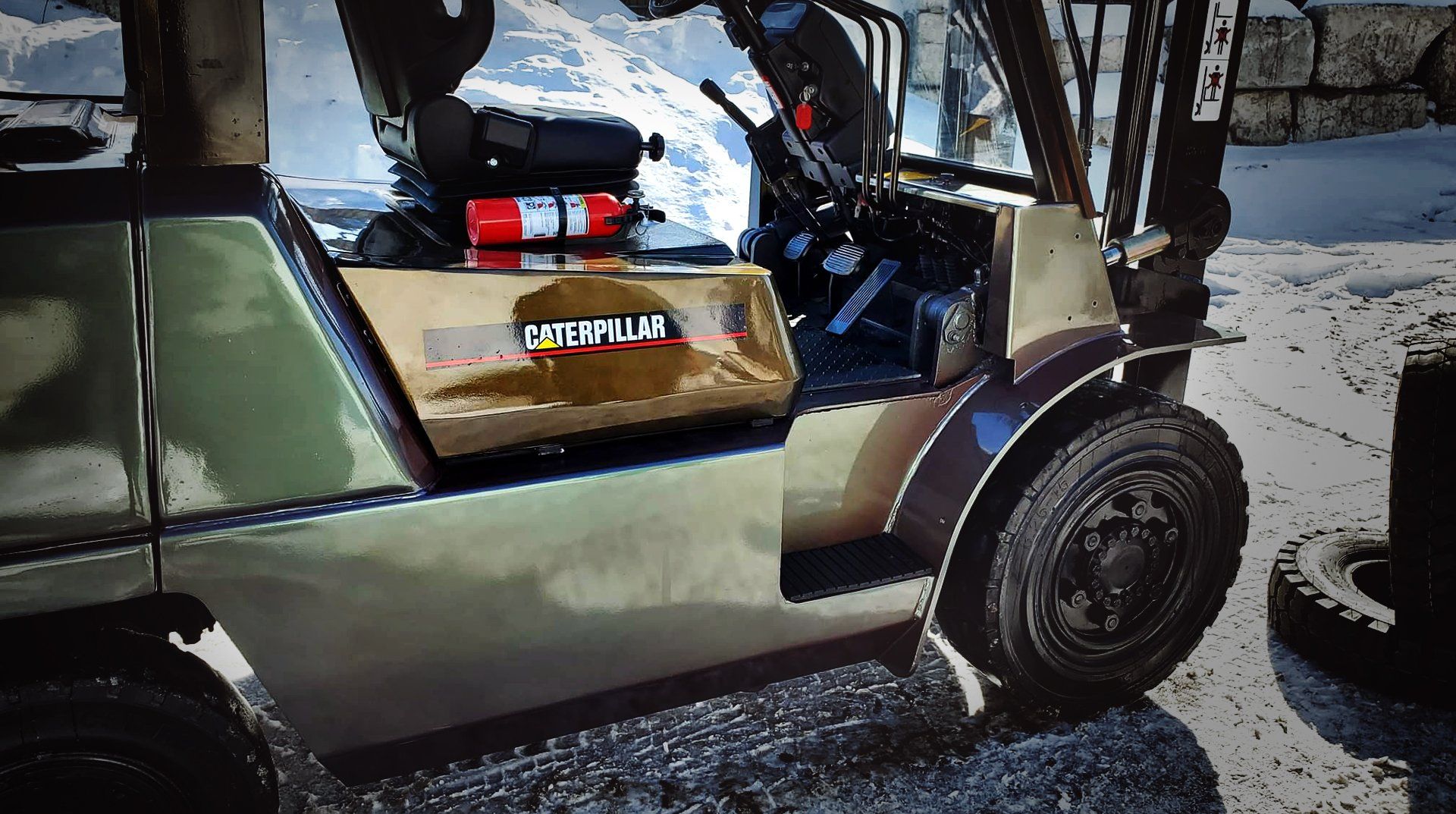 Un chariot élévateur avec un logo « Caterpillar », conduit par une personne en tenue de camouflage, dans un environnement enneigé.