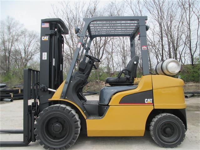 A yellow cat forklift is parked in a dirt lot