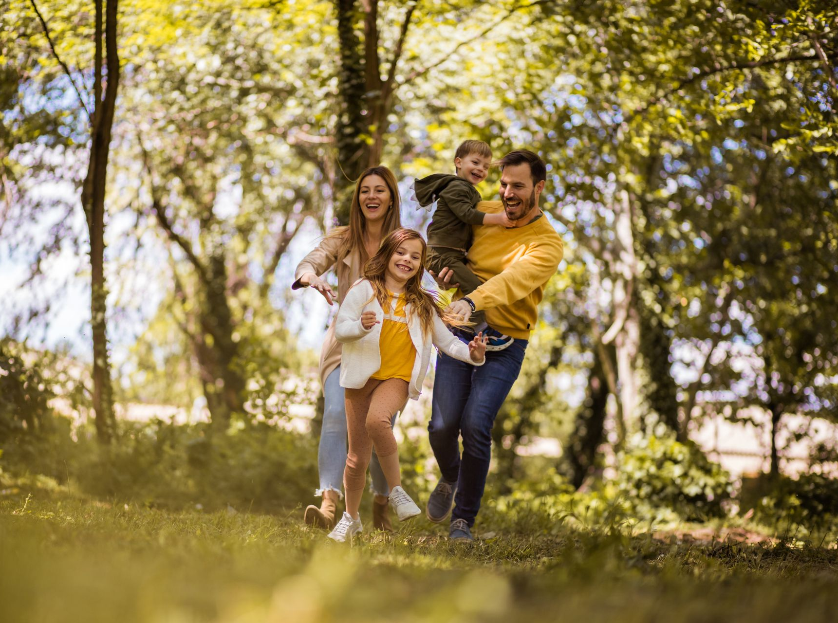 Family running together in a park with trees, smiling.