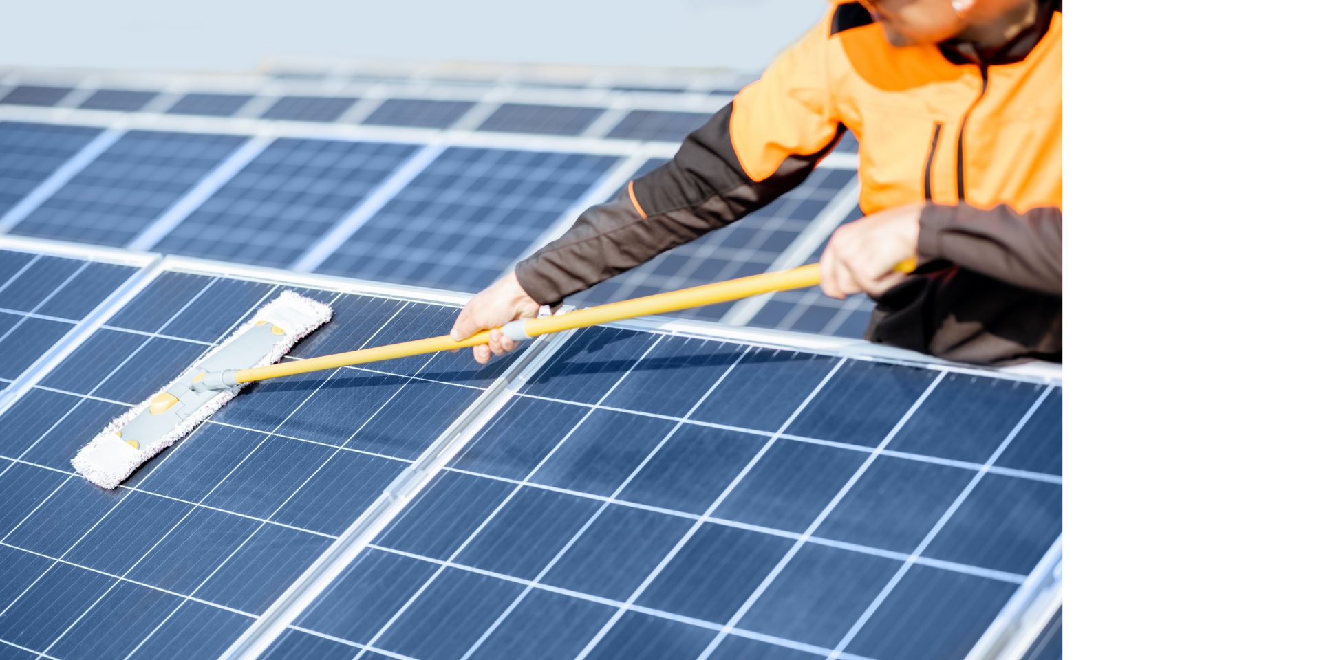 Person cleaning solar panels with a long-handled squeegee. Orange and black jacket. Blue panels.