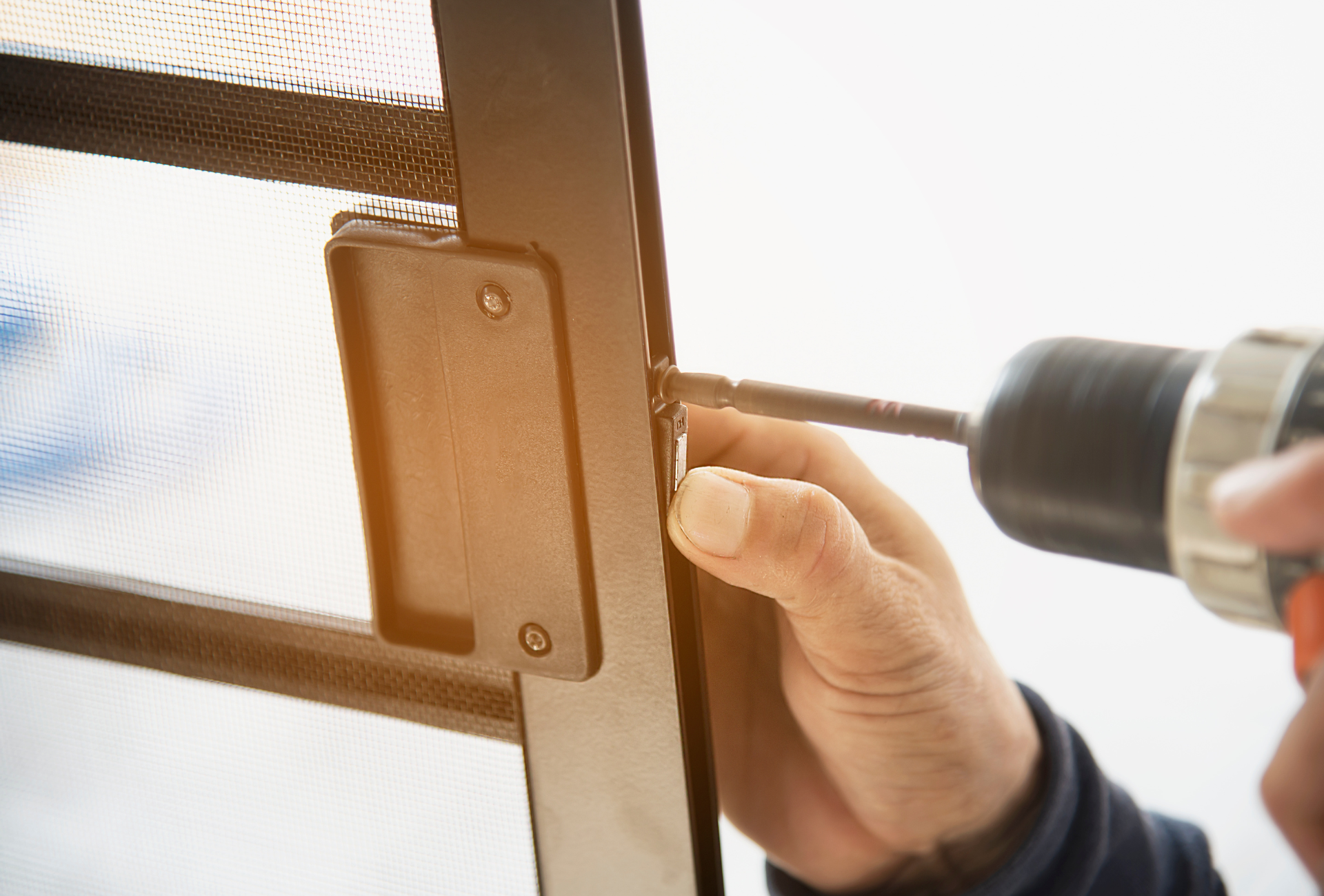 A person is using a drill to fix a screen door.