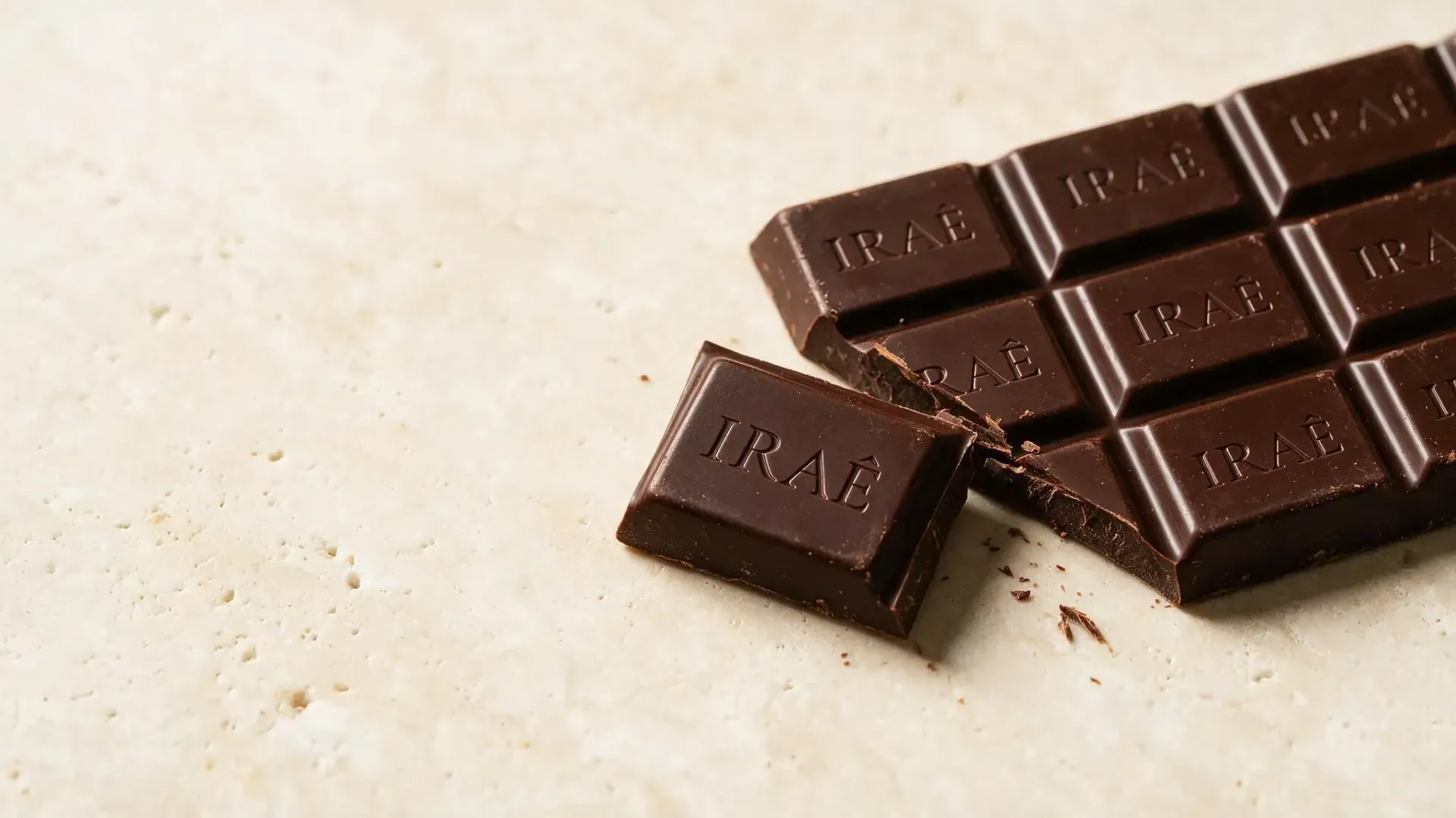 Pedaços de chocolate amargo sobre uma superfície clara, com um pedaço quebrado em primeiro plano.