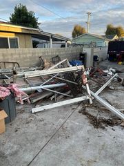 A collapsed white metal patio cover structure lying in a debris-filled residential backyard.