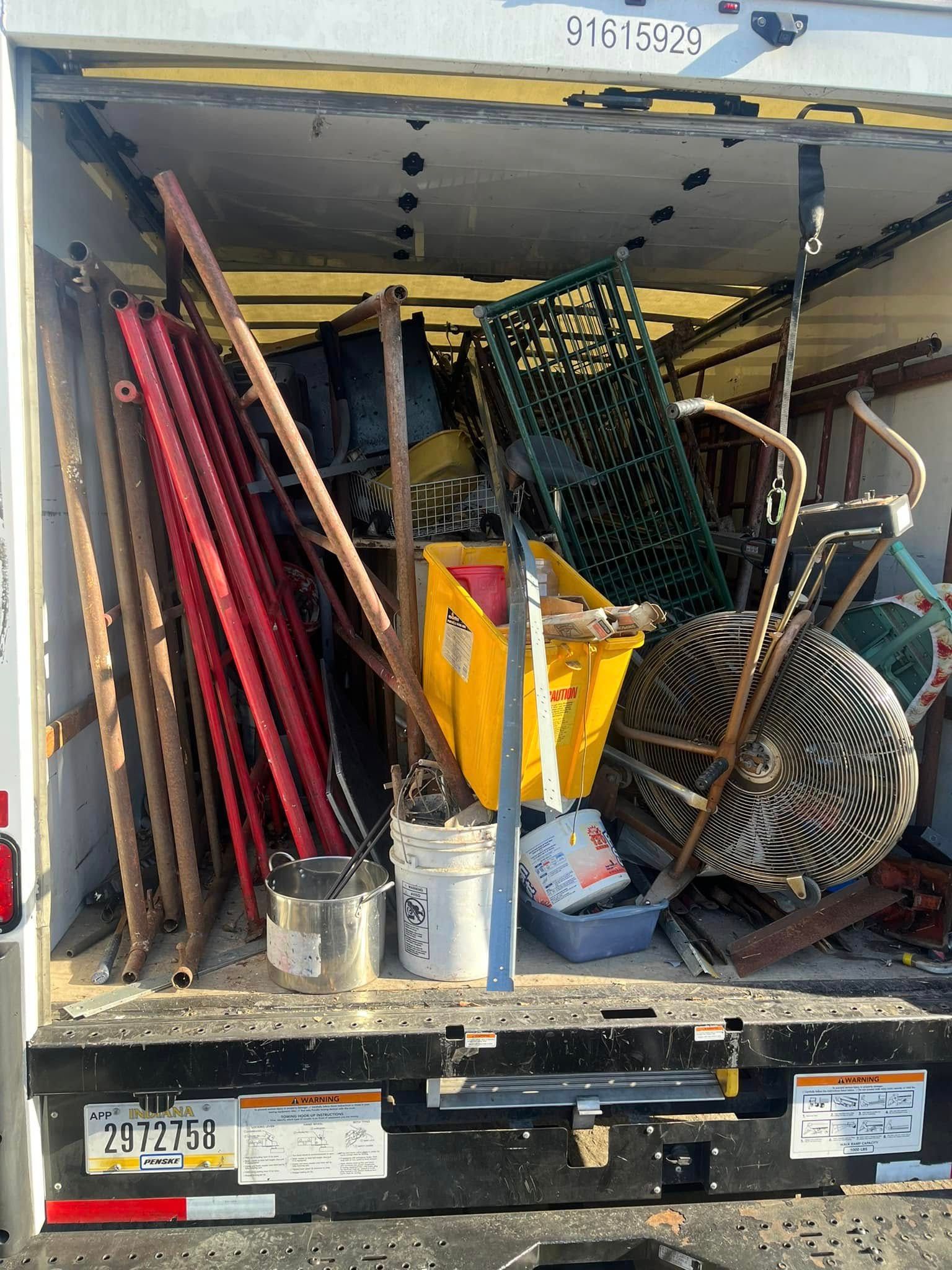 The open back of a moving truck packed with miscellaneous items, including red bed frames, a yellow bin, and a treadmill.