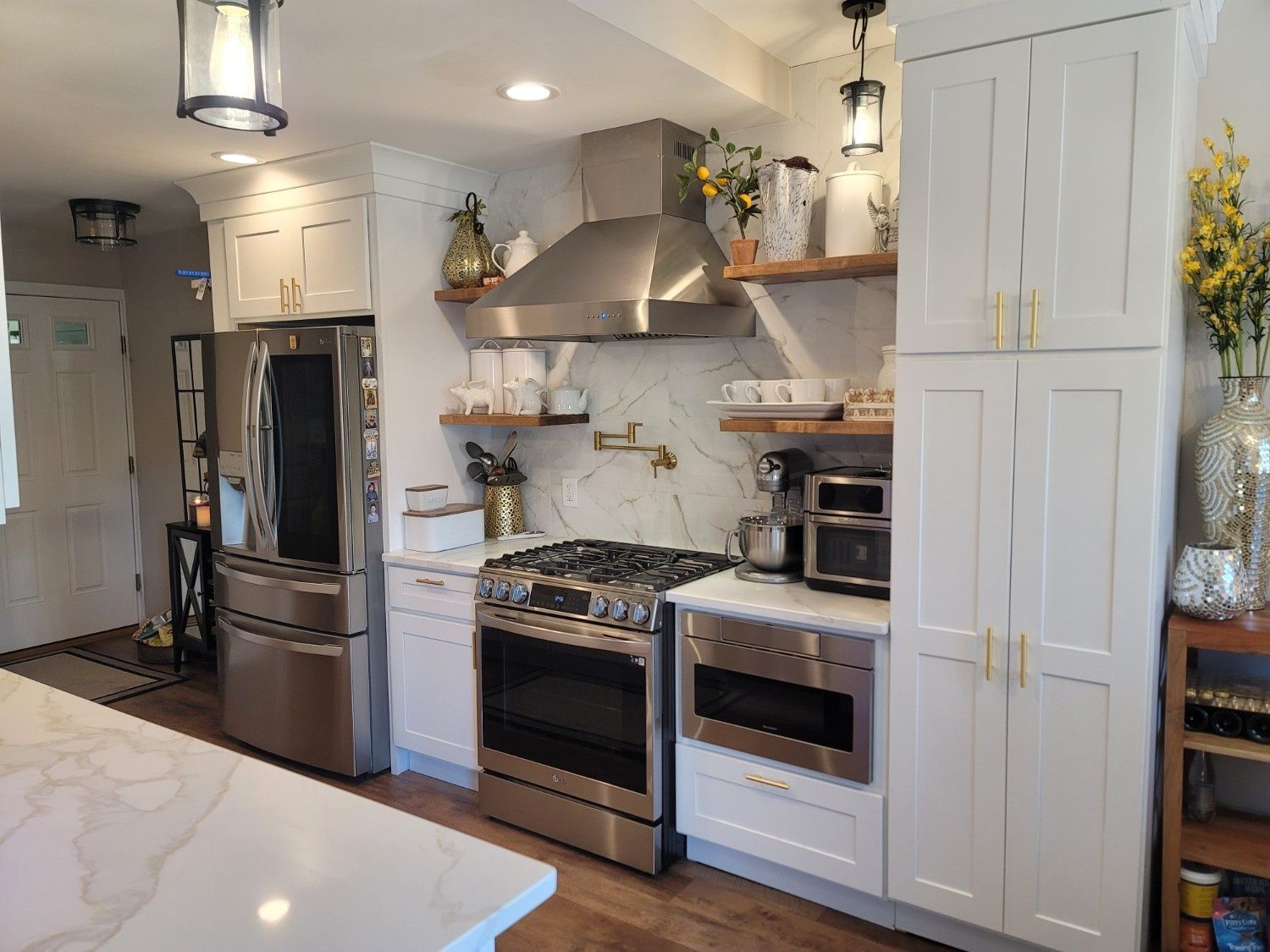 A bright, modern kitchen features white cabinets, marble countertops, stainless steel appliances, and gold hardware.
