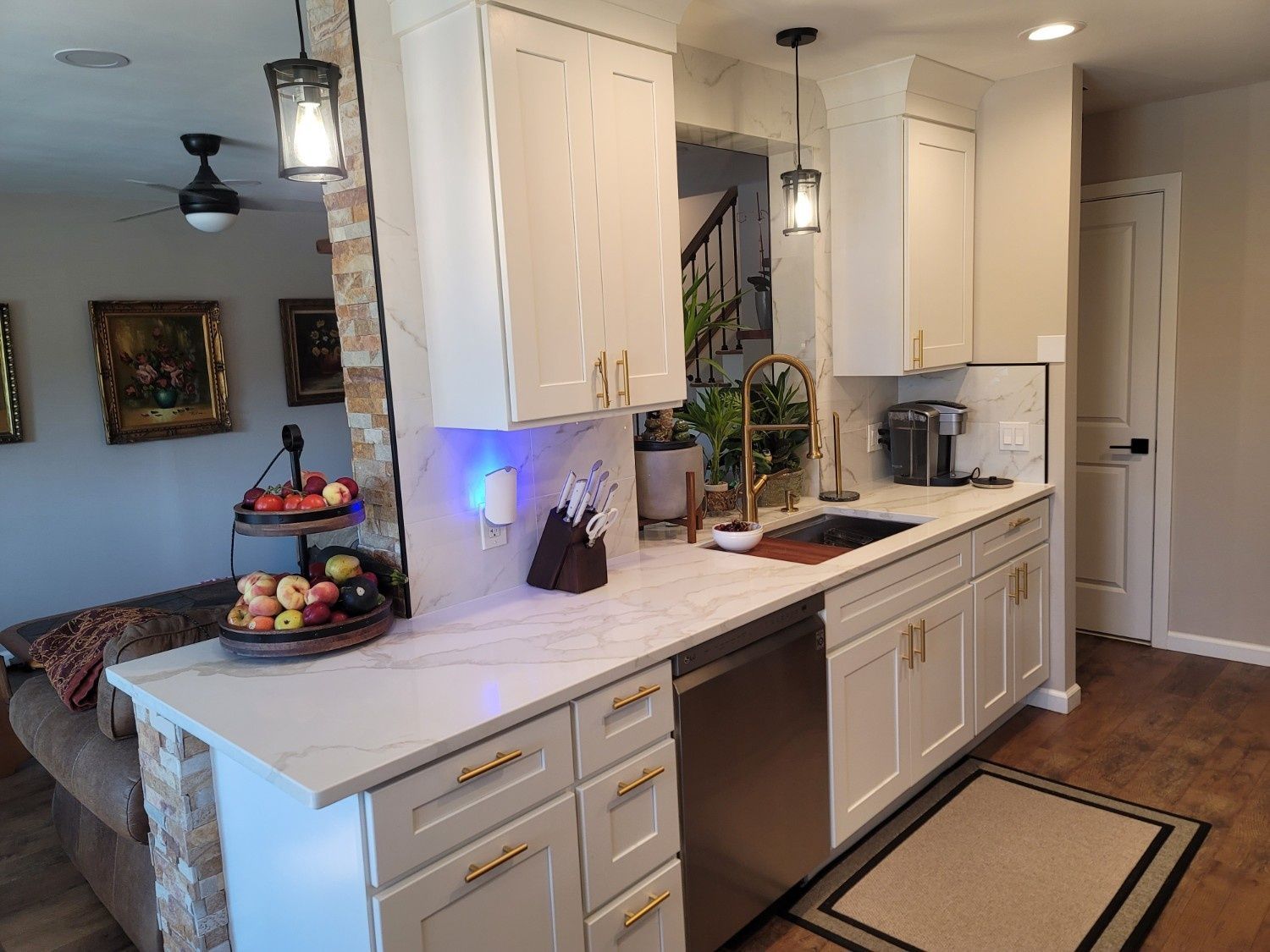 A modern kitchen featuring white cabinets, stone-accented counters, gold hardware, and stainless steel appliances.