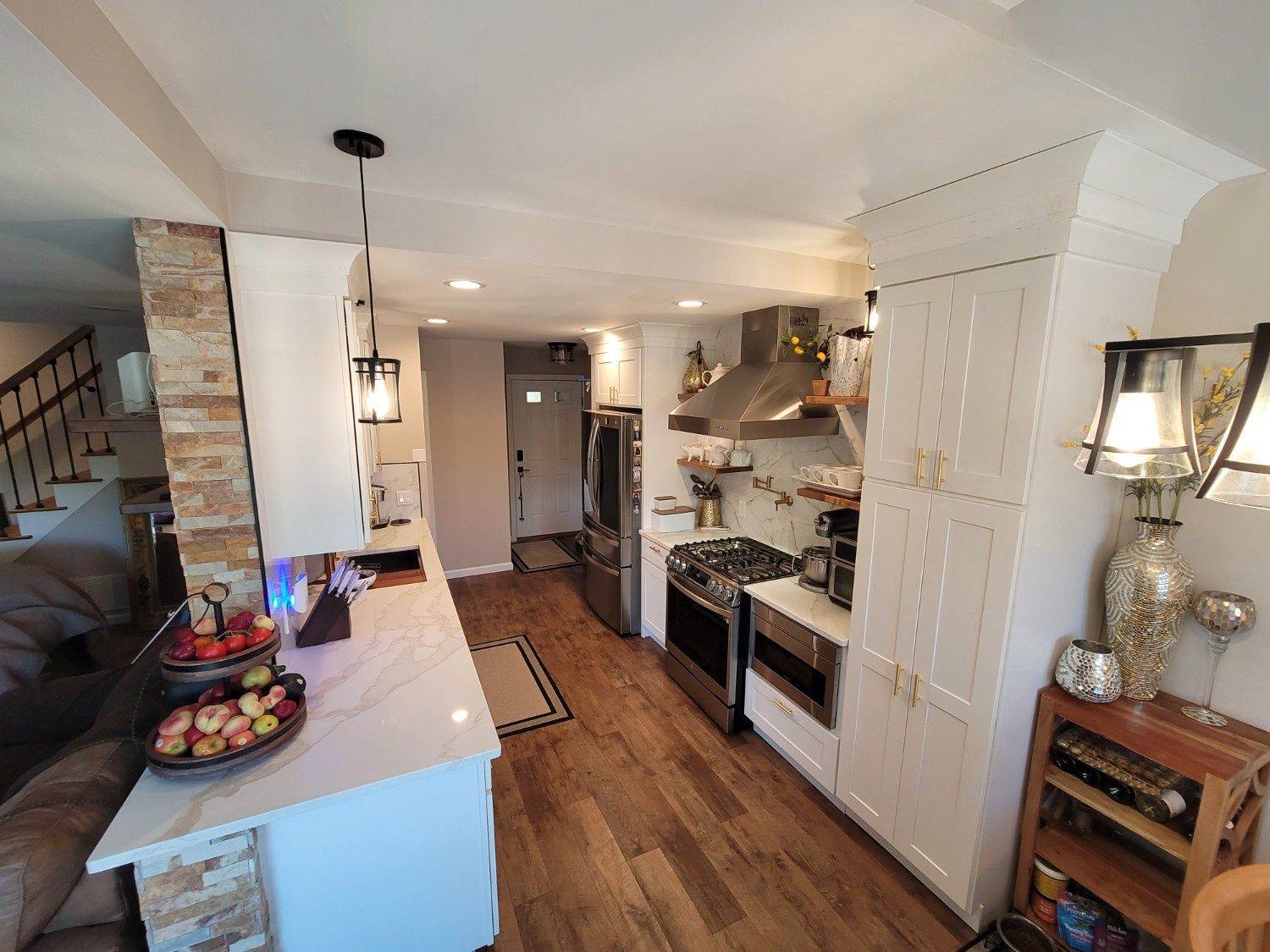 A modern kitchen with white cabinetry, stainless steel appliances, a stone-accented island, and light wood flooring.