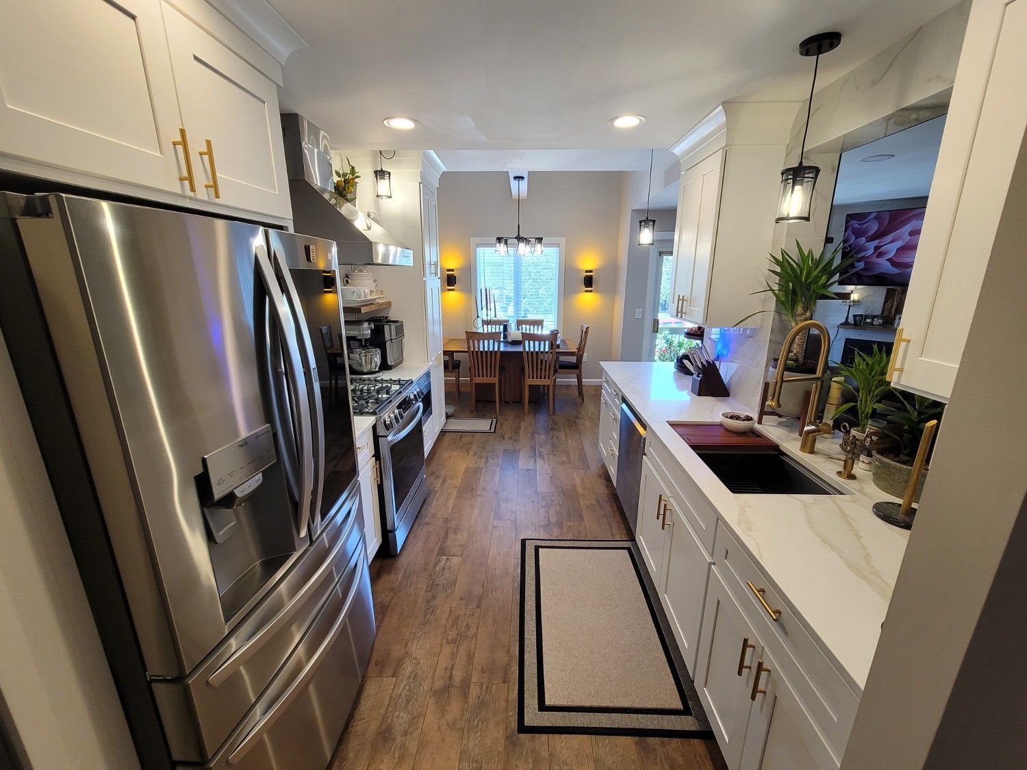 A modern kitchen with white cabinetry, stainless steel appliances, and wood floors leading to a dining area with a table.