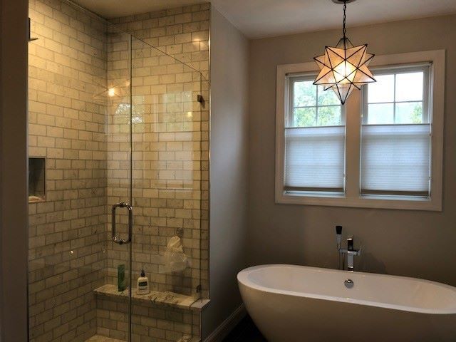 A modern bathroom with a glass-enclosed subway tile shower, a freestanding white tub, and a star-shaped pendant light.