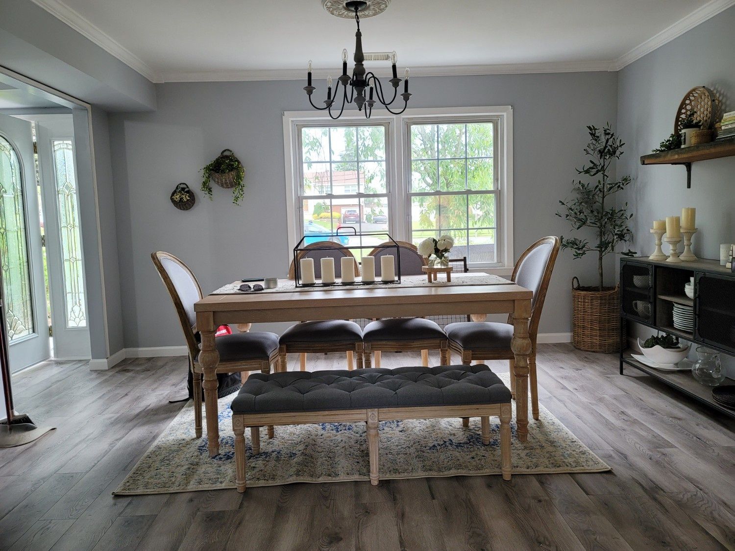 A dining room with a wooden table, dark upholstered chairs, a tufted bench, a chandelier, and a side console on wood floors.