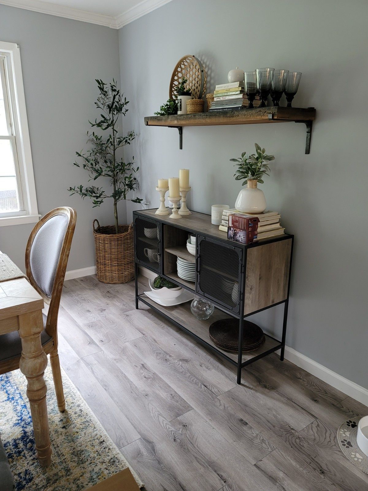 A gray-walled room features a wooden console table with metal mesh doors, topped with candles, decor, and a wall shelf.